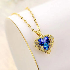 A gold-tone necklace featuring a heart-shaped blue crystal pendant framed by angel wings.