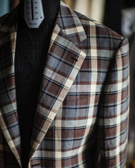 A brown and blue plaid blazer with a notch lapel worn over a black textured shirt.