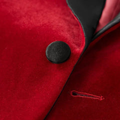 A close-up of a red velvet tuxedo blazer featuring a black peak lapel and a single button.