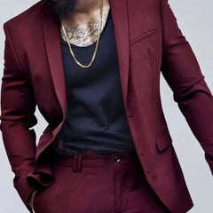 A man wears a burgundy slim-fit single-breasted suit with a black undershirt and gold chain.