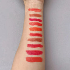 Ten different shades of matte lipstick are swatched in horizontal lines on a person's forearm.