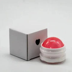 A pink manual massage roller ball sits next to its small white cardboard packaging box.