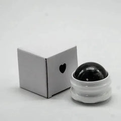 A manual massage roller ball with a black sphere and a white base next to a small white box.