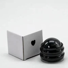 A black manual massage roller ball sits next to its small white box with a heart cutout.