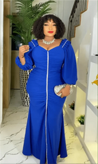 A woman wears a royal blue, long-sleeved maxi dress with a central silver trim and ruched detailing.
