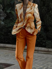 A person wears a two-piece suit featuring a tan marbled print blazer and solid orange trousers.
