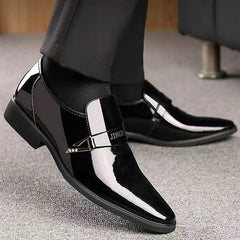 A pair of black patent leather slip-on loafers for men with a decorative metal side accent.