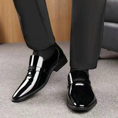 A pair of black glossy slip-on loafers for men with a branded strap across the vamp.