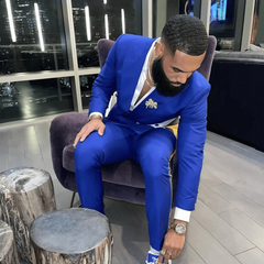 A man wears a slim-fit blue double-breasted suit with white lapel accents and matching trousers.