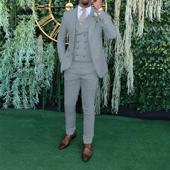A man wearing a light gray three-piece suit with a double-breasted vest and brown dress shoes.