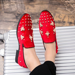 A pair of red corduroy slip-on dress shoes decorated with gold bee emblems and metal studs.