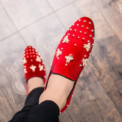 A pair of red corduroy slip-on loafers decorated with gold bee emblems and metal studs.