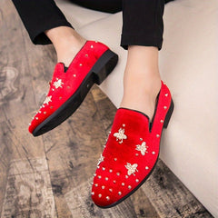 A pair of red corduroy slip-on loafers decorated with gold bee emblems and metal studs.