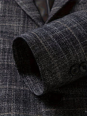 A close-up of a dark grey plaid blazer sleeve featuring a notched lapel and button details.
