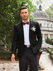 A man wears a black floral paisley tuxedo jacket with a shawl lapel and a burgundy bow tie.