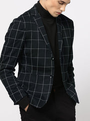 A man wears a black lightweight blazer featuring a white grid pattern over a black turtleneck.