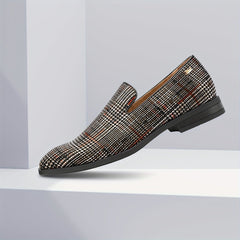 A men's slip-on loafer featuring a black and white plaid pattern with a round toe and black sole.