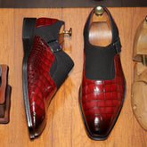 A pair of red crocodile-patterned monk strap dress shoes with black elastic side panels.