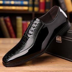 A sleek black men's dress shoe with a crocodile-textured lace-up design and a pointed toe.