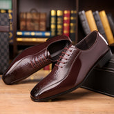 A pair of glossy brown lace-up dress shoes with a crocodile texture and pointed toe.