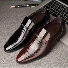 A pair of black and brown crocodile-embossed slip-on dress shoes with pointed toes.