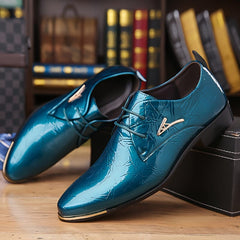 A pair of glossy teal men's lace-up dress shoes with gold accents on a wooden surface.