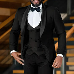 A man wears a black slim-fit three-piece tuxedo with a shawl lapel and a matching bow tie.