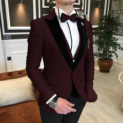 A man wears a burgundy three-piece tuxedo with a black velvet shawl lapel and a matching bow tie.