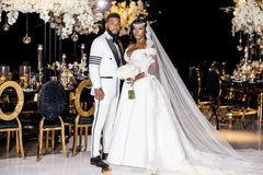 A man wears a white slim-fit tuxedo with black lapels and sleeve stripes next to a bride.
