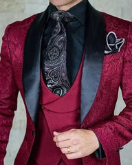 A burgundy patterned three-piece suit featuring a black shawl lapel, black shirt, and paisley tie.