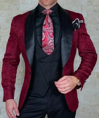 A man wears a burgundy patterned tuxedo jacket with a black shawl lapel, vest, and paisley tie.