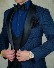 A man wears a navy blue patterned three-piece tuxedo with a black shawl lapel and bow tie.