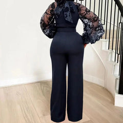 A woman wears a black jumpsuit with long sheer lace sleeves and wide-leg trousers.