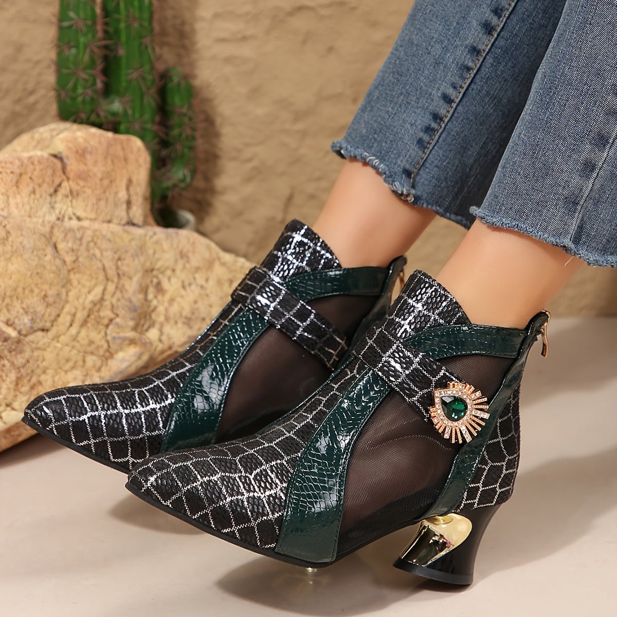 A pair of black mesh pointed-toe ankle boots with a green crocodile-textured strap and gold heel.