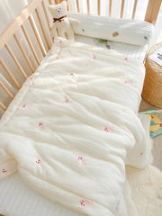 A white muslin baby blanket featuring a small pink bunny pattern draped over a crib.