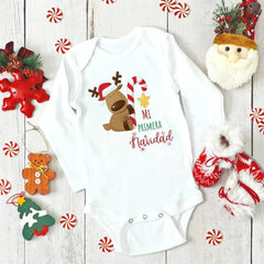 A white long-sleeved baby bodysuit featuring a reindeer graphic and the text Mi Primera Navidad.