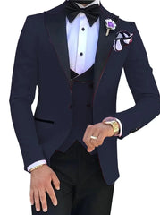 A man wears a slim-fit navy blue three-piece suit with a black bow tie and a floral lapel pin.