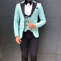 A man wears a mint green three-piece suit with black lapels, a black bowtie, and black trousers.