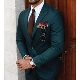A man wears a slim-fit dark green two-piece suit with a white shirt and brown knit tie.