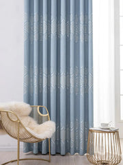 A blue blackout curtain with a silver geometric pattern hangs in a modern living room.