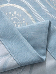 A close-up view of a blue fabric curtain with a subtle textured pattern and a folded edge.