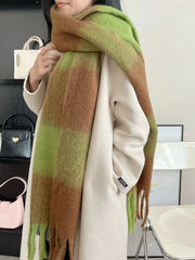 A person wears a soft, oversized green and brown plaid scarf over a cream-colored coat.