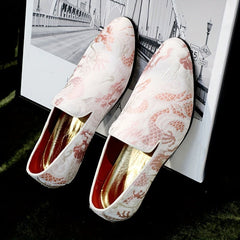 A pair of men's slip-on shoes featuring a white fabric upper with intricate pink embroidery.