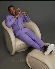 A man wearing a slim-fit, double-breasted purple suit with gold buttons while sitting in a chair.
