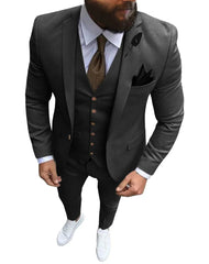 A man wears a dark grey three-piece slim fit suit with a brown tie and white sneakers.