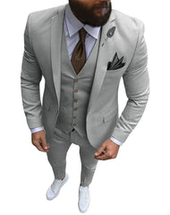 A man wearing a light gray three-piece slim fit suit with a brown tie and white sneakers.