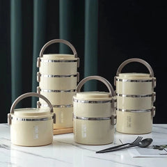 Four beige, stackable stainless steel thermal lunch boxes of varying heights on a marble surface.