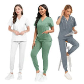 Three women wearing matching scrub sets with V-neck tops and jogger-style pants in different colors.