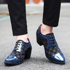 A pair of blue and black patterned lace-up dress shoes with a block heel worn with black trousers.