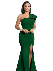 A woman wears a floor-length, emerald green one-shoulder mermaid dress with a side slit and ruffle.